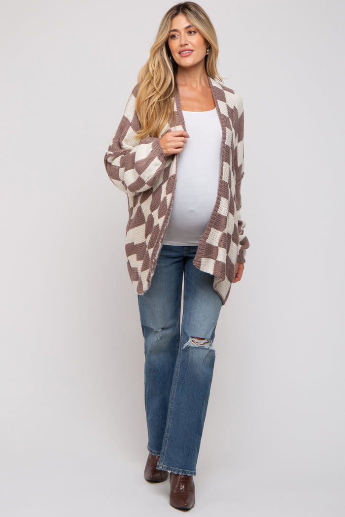 woman wearing a brown and white checkered maternity cardigan over a white top and blue jeans, showing her baby bump