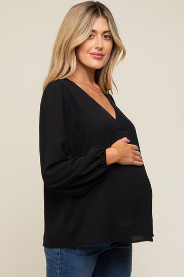 woman wearing a black maternity top with a deep v-neck and long sleeves, holding her baby bump