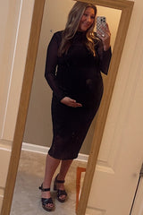 woman wearing a black fitted maternity dress with long sleeves and a baby bump, posing in front of a mirror