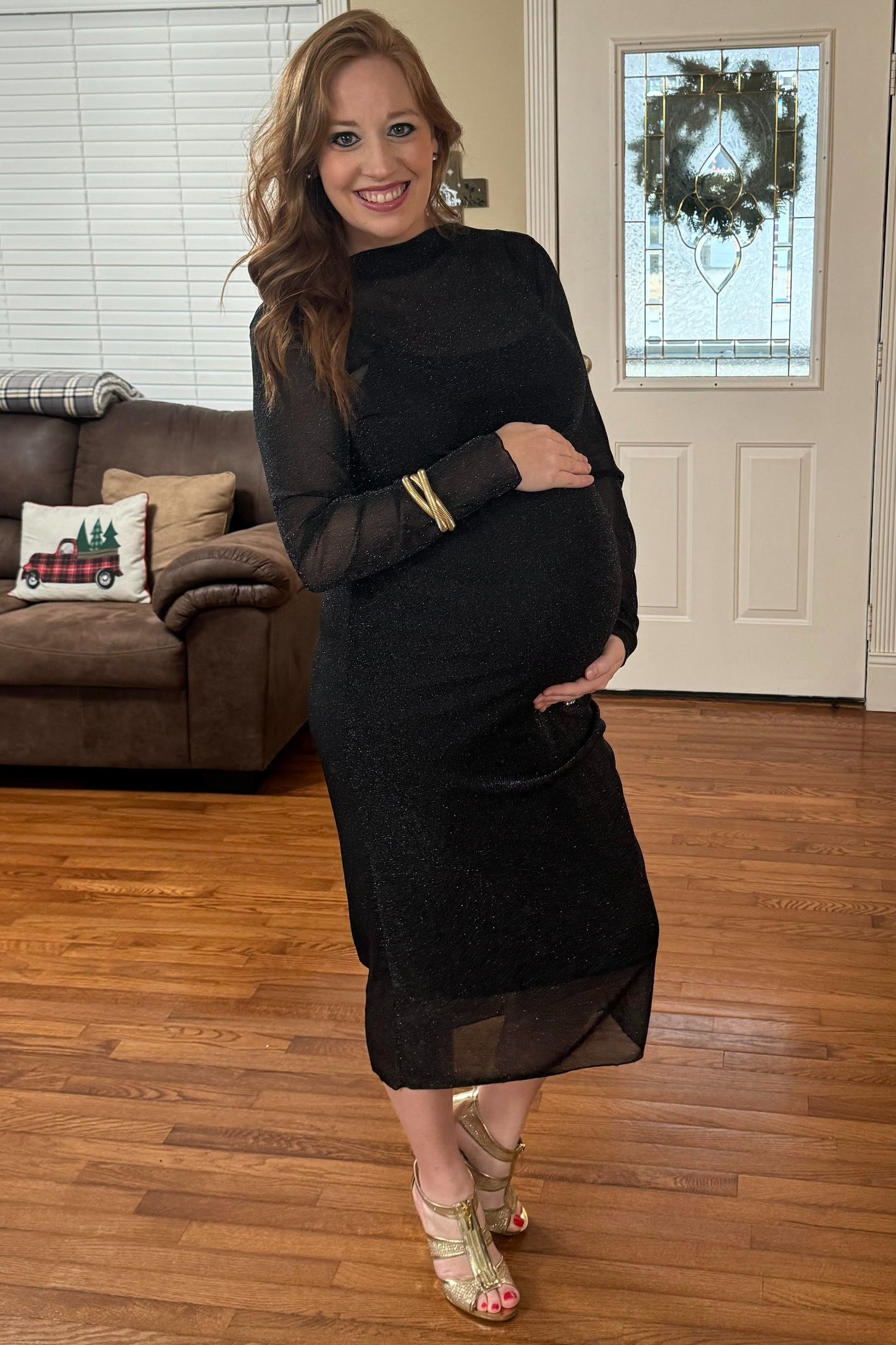 woman wearing a black sparkly maternity dress and highlighting her baby bump while standing indoors