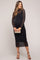 woman wearing a black long sleeve maternity dress with ruched detailing and holding a small clutch, showing her baby bump