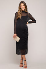 woman wearing a black ruched maternity dress with sheer long sleeves and holding a clutch purse, visible baby bump