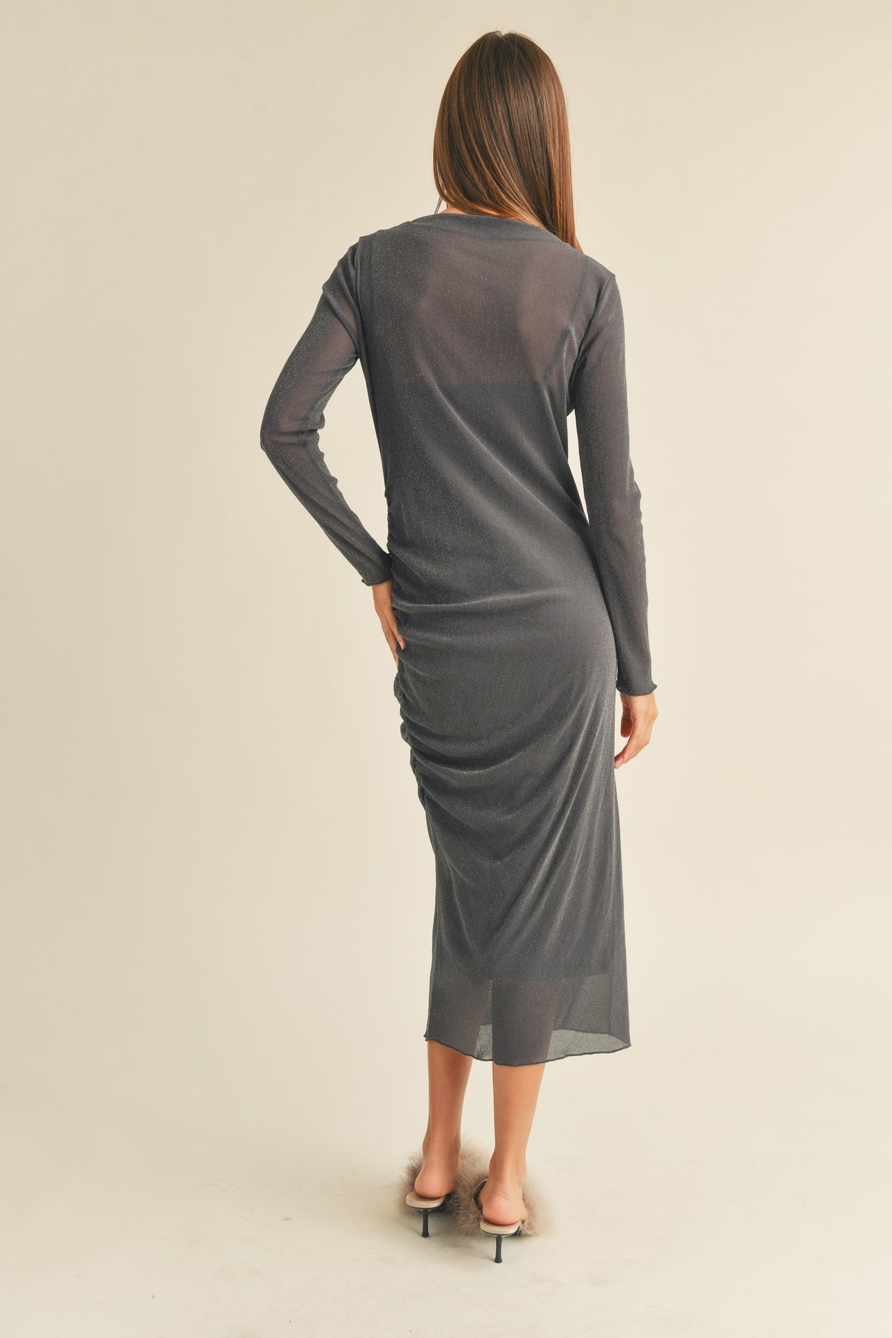 woman wearing a fitted charcoal gray long sleeve midi dress with ruching details at the back