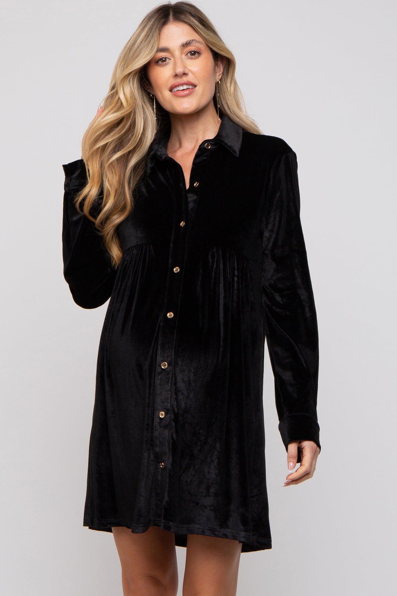 woman wearing a black velvet button-up maternity dress with a slightly flared silhouette and long sleeves, showing baby bump