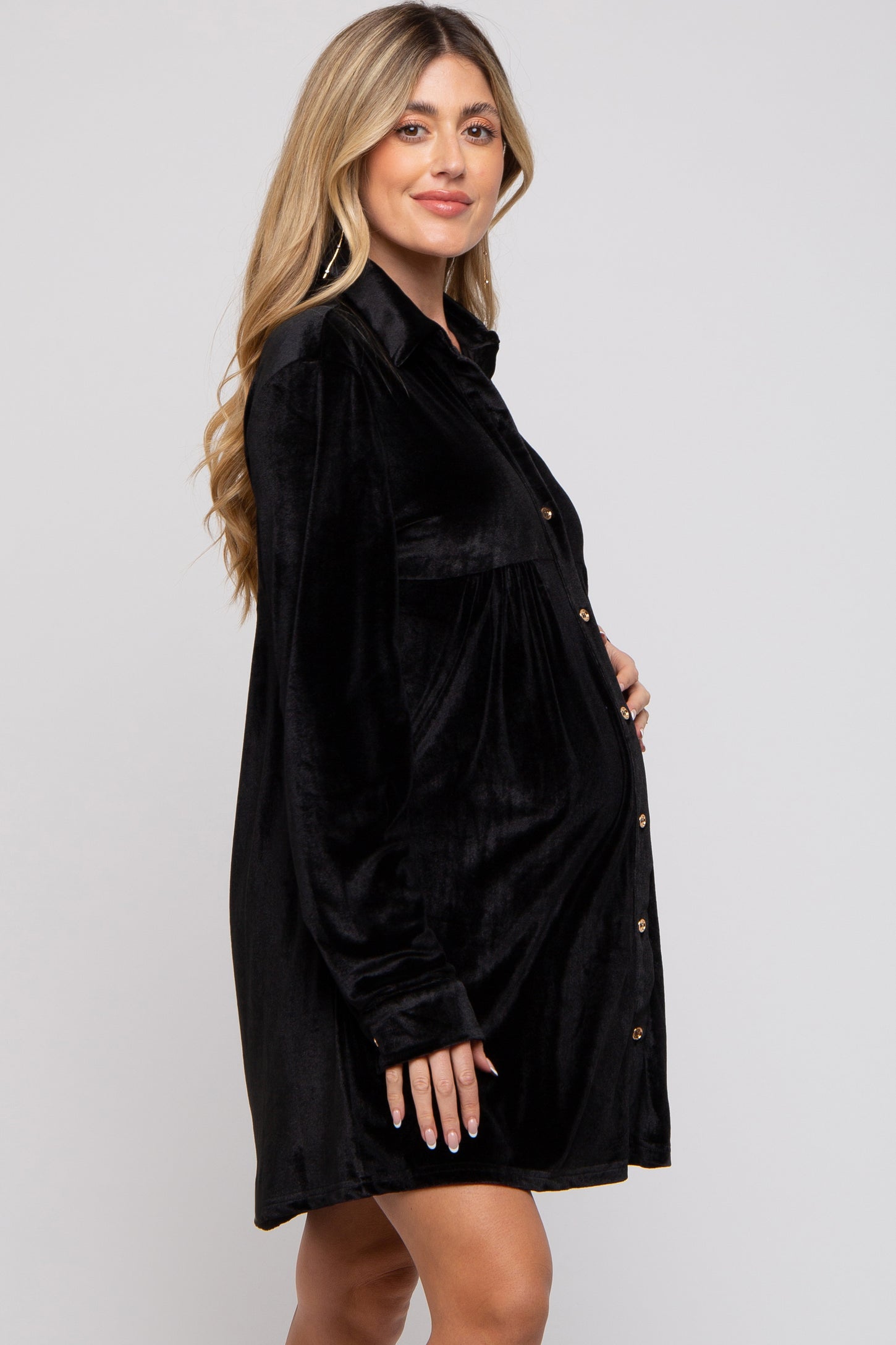 woman wearing a black velvet maternity shirt dress, standing with a visible baby bump