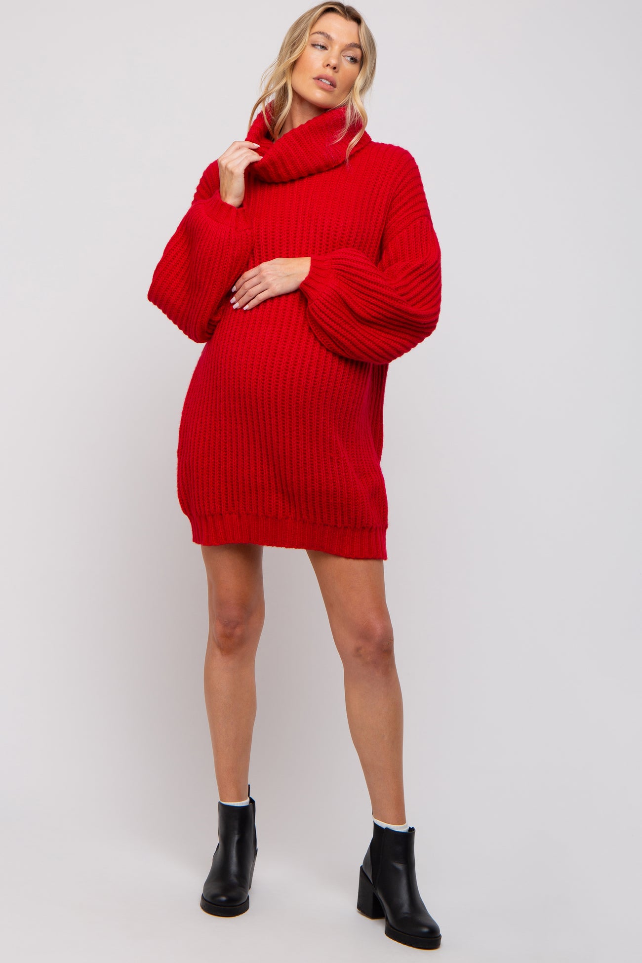 woman wearing a red oversized knitted maternity sweater with a cowl neck and holding her baby bump