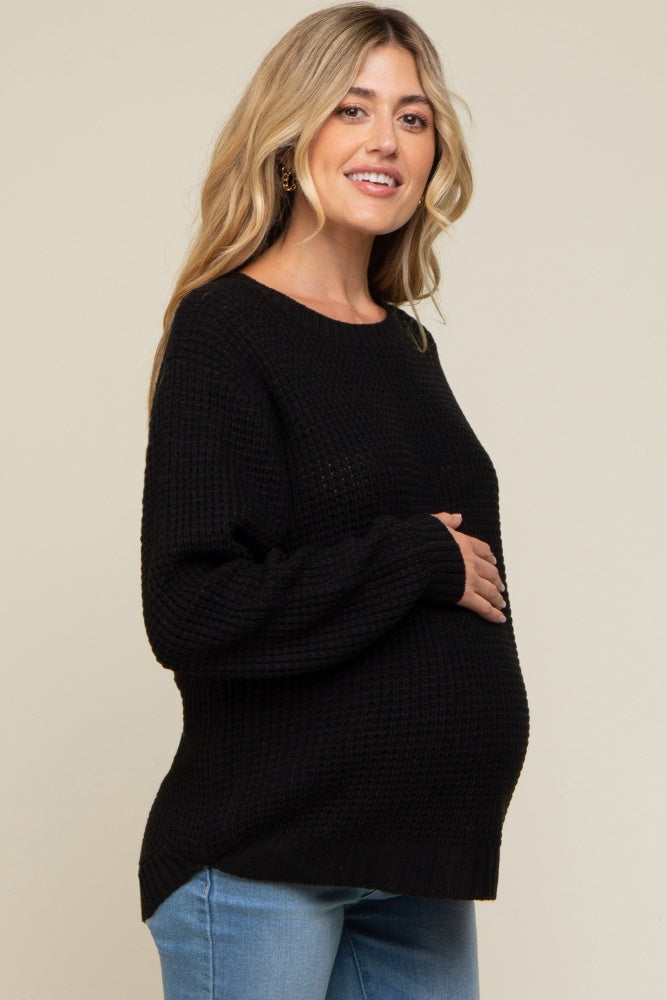 woman wearing a black maternity sweater and cradling her baby bump