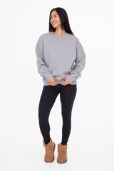 woman wearing a gray oversized sweatshirt, black leggings, and brown ankle boots, standing and smiling