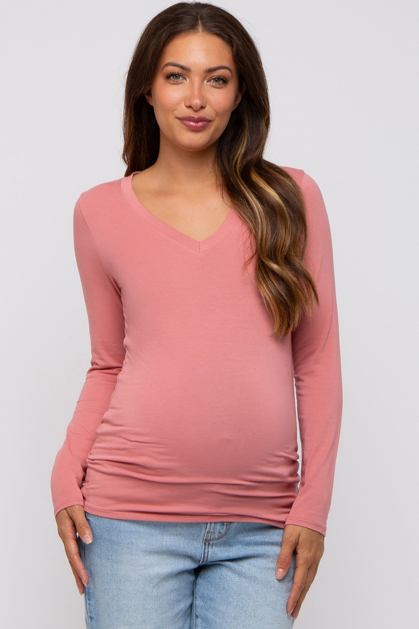 woman wearing a pink long sleeve maternity top with a v-neck and visible baby bump