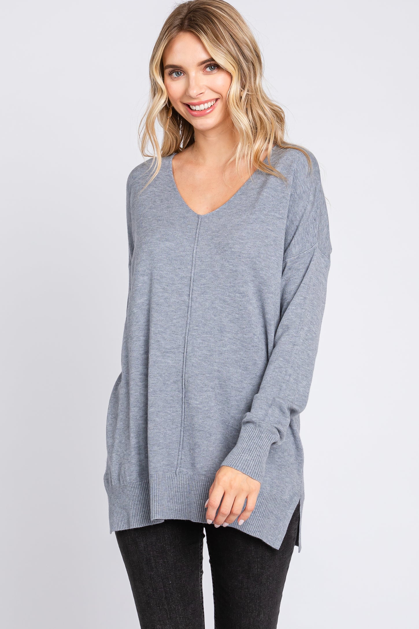 woman wearing a gray oversized v-neck sweater with side slits and long sleeves, smiling at the camera