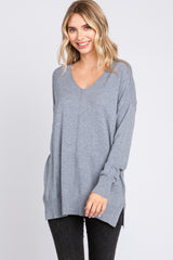 woman wearing a gray oversized v-neck sweater with side slits and long sleeves, smiling at the camera
