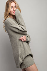 woman wearing a light olive green oversized sweater and matching shorts, smiling and posing sideways