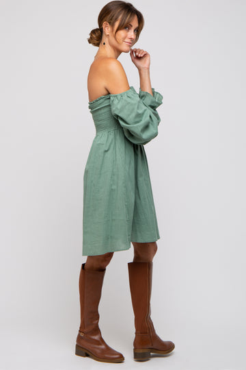 woman wearing a green off-the-shoulder smocked dress with long sleeves and brown knee-high boots