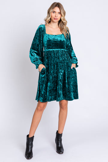 woman wearing a teal velvet long sleeve dress with a square neckline and pockets