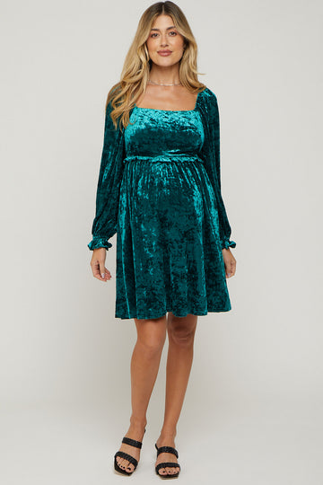woman wearing a teal velvet maternity dress with long sleeves and a fitted waist, showing her baby bump