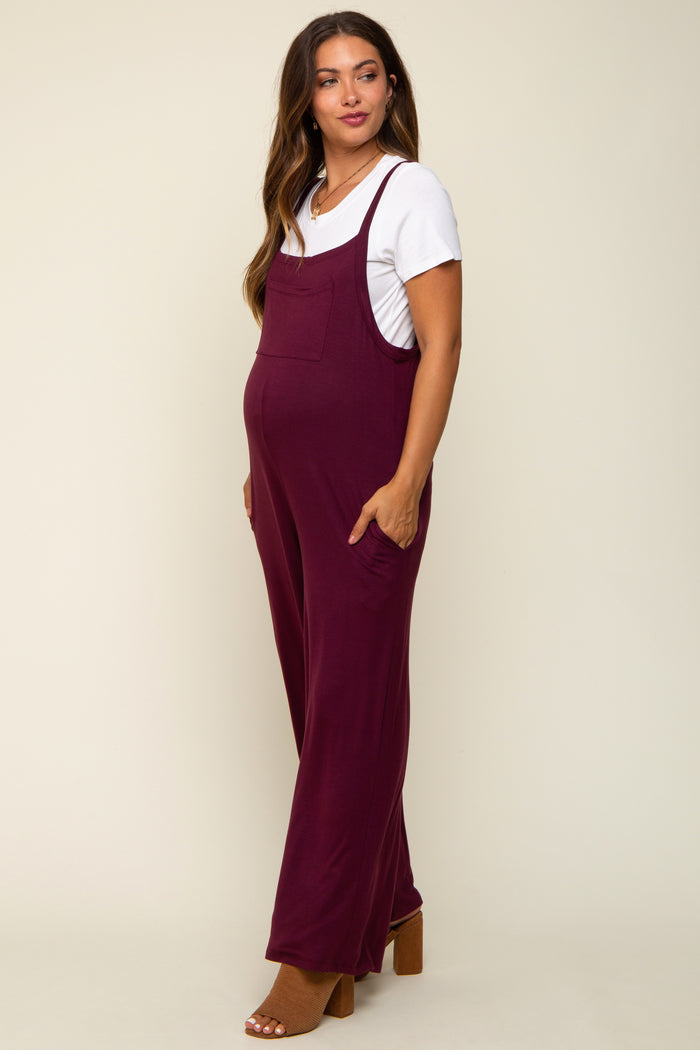 woman wearing a burgundy maternity jumpsuit with pockets and a white t-shirt, showcasing her baby bump