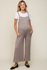 woman wearing a light brown maternity jumpsuit with pockets over a white t-shirt and showing a baby bump