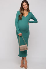woman wearing a green ribbed maternity dress with a v-neckline and a visible baby bump, holding a handbag