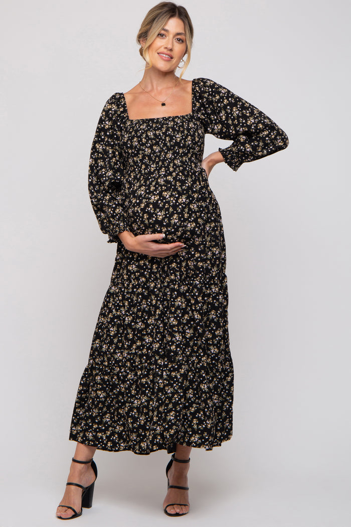 woman wearing a black floral maternity maxi dress with long puff sleeves and holding her baby bump