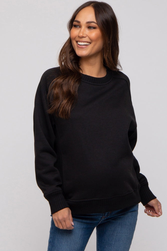 woman wearing a black maternity sweatshirt and smiling, showcasing her baby bump with blue jeans