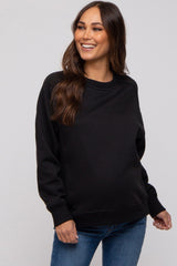 woman wearing a black maternity sweatshirt and smiling, showcasing her baby bump with blue jeans