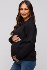 woman wearing a black maternity sweatshirt and gently holding her baby bump