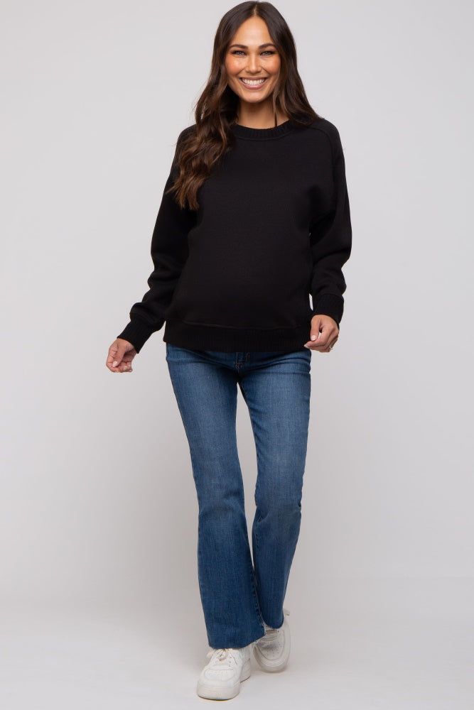 woman wearing a black maternity sweatshirt and blue flared jeans, smiling with a baby bump visible