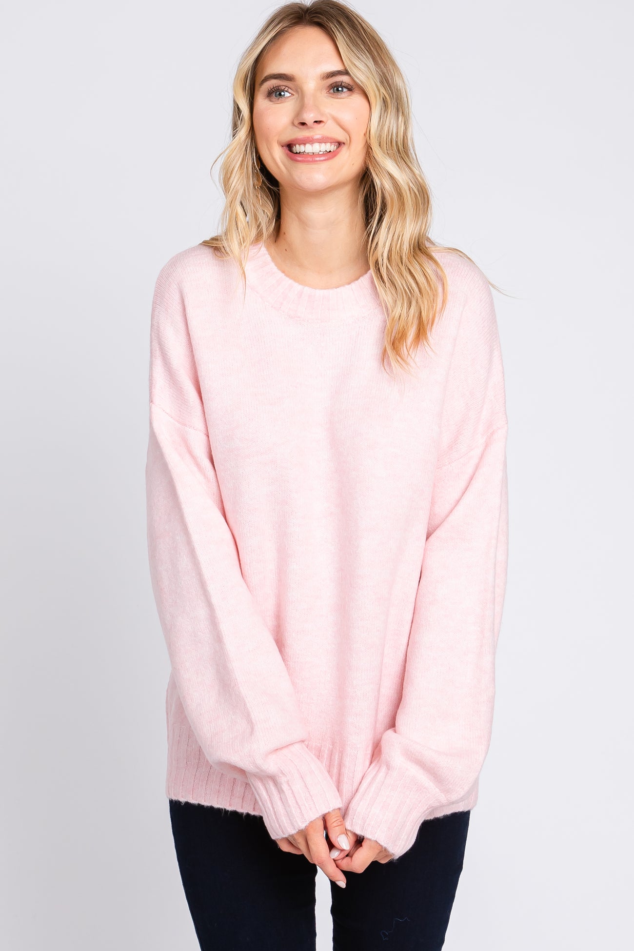woman wearing a soft pink oversized sweater with long sleeves and ribbed hem, smiling at the camera
