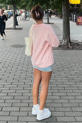 woman wearing a light pink oversized sweater and denim shorts, paired with white sneakers and a hair scrunchie