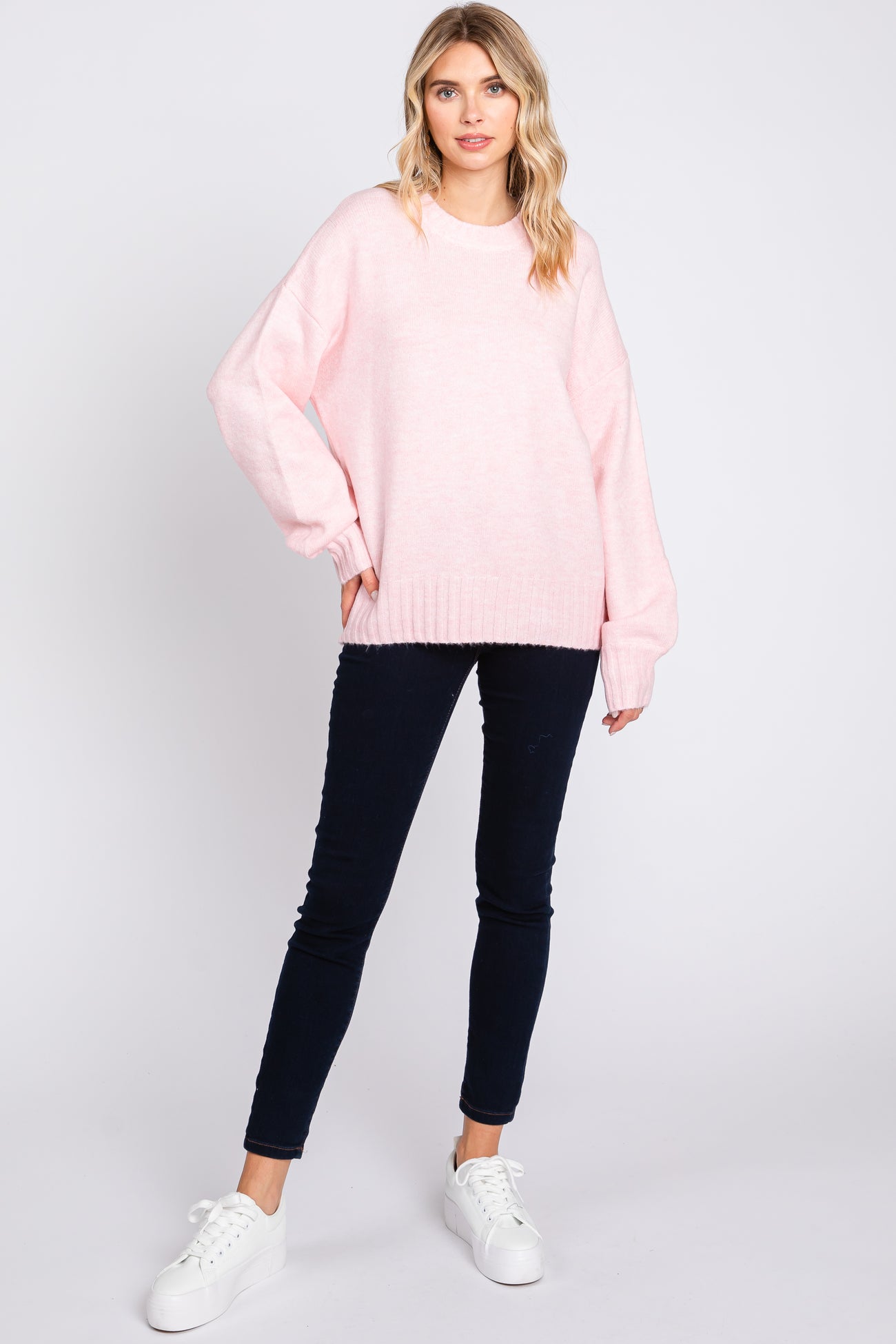 woman wearing a light pink oversized sweater with long sleeves and paired with dark skinny jeans and white sneakers