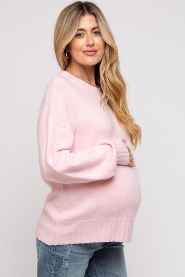 woman wearing a light pink oversized maternity sweater and holding her baby bump