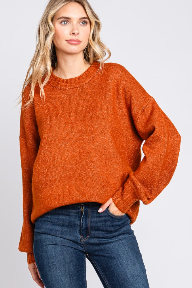 woman wearing an oversized orange sweater with a ribbed neckline and long sleeves, styled with dark blue jeans