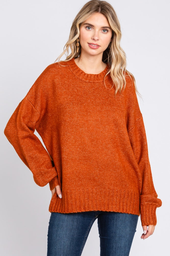 woman wearing an orange oversized sweater with a round neckline and relaxed fit, paired with blue jeans