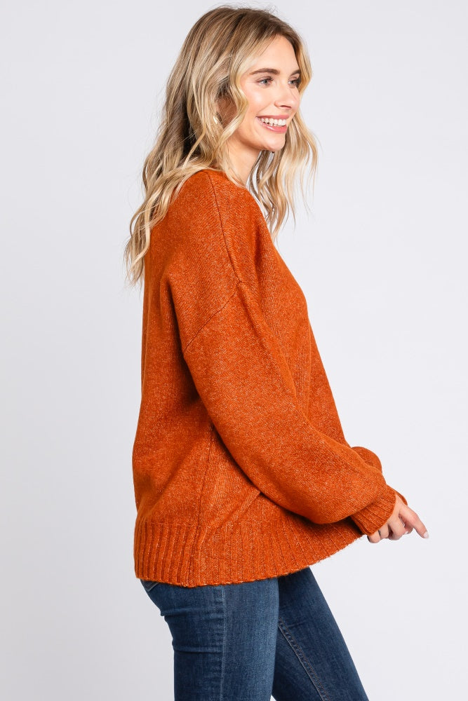 woman wearing an oversized bright orange sweater with long sleeves and a textured knit design, smiling to the side