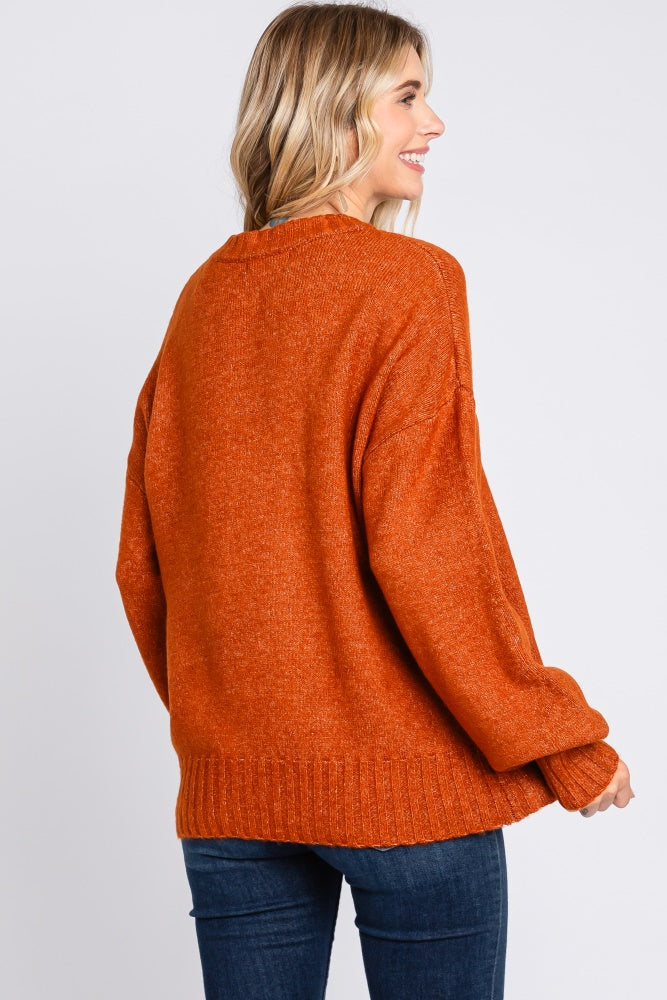 woman wearing an oversized orange knit sweater, showing the back view, paired with dark blue jeans