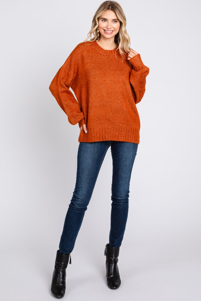 woman wearing an oversized rust orange knit sweater with long sleeves and blue skinny jeans, posing in black ankle boots