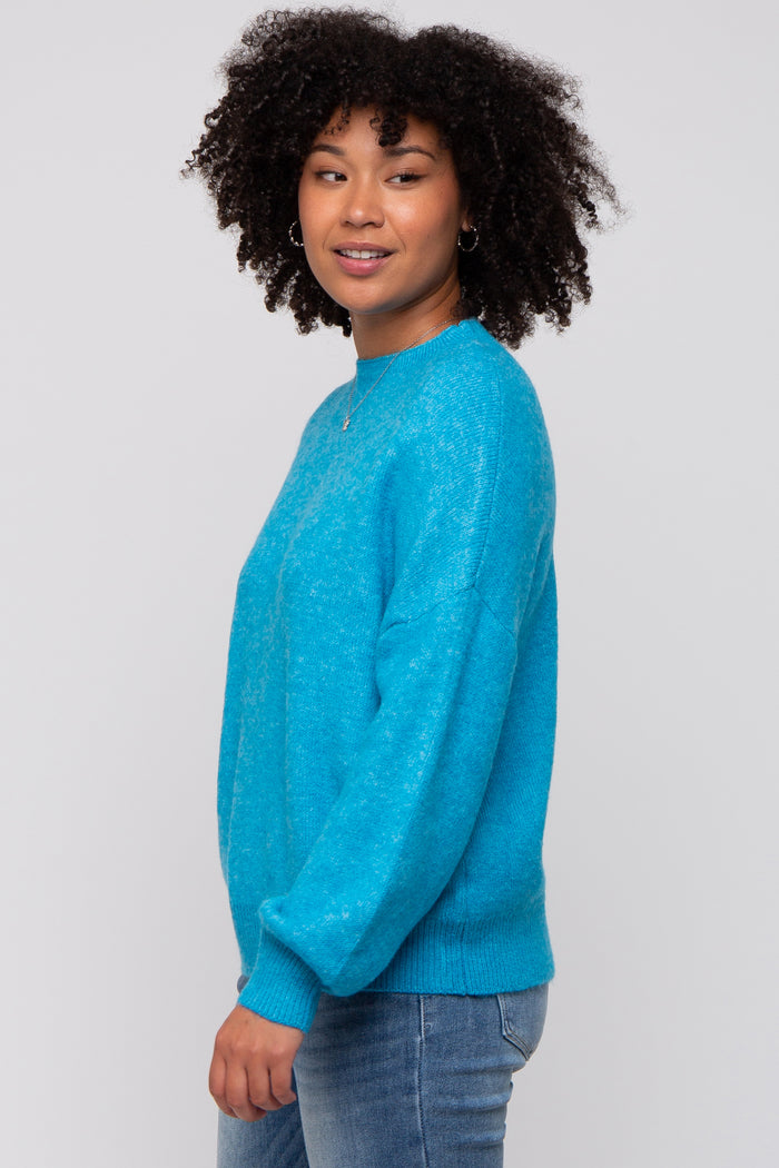 woman wearing a bright turquoise cozy sweater with long sleeves and a relaxed fit, posing sideways