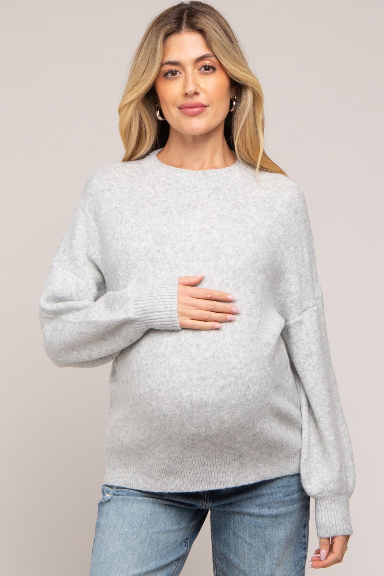 woman wearing a light gray maternity sweater and holding her baby bump