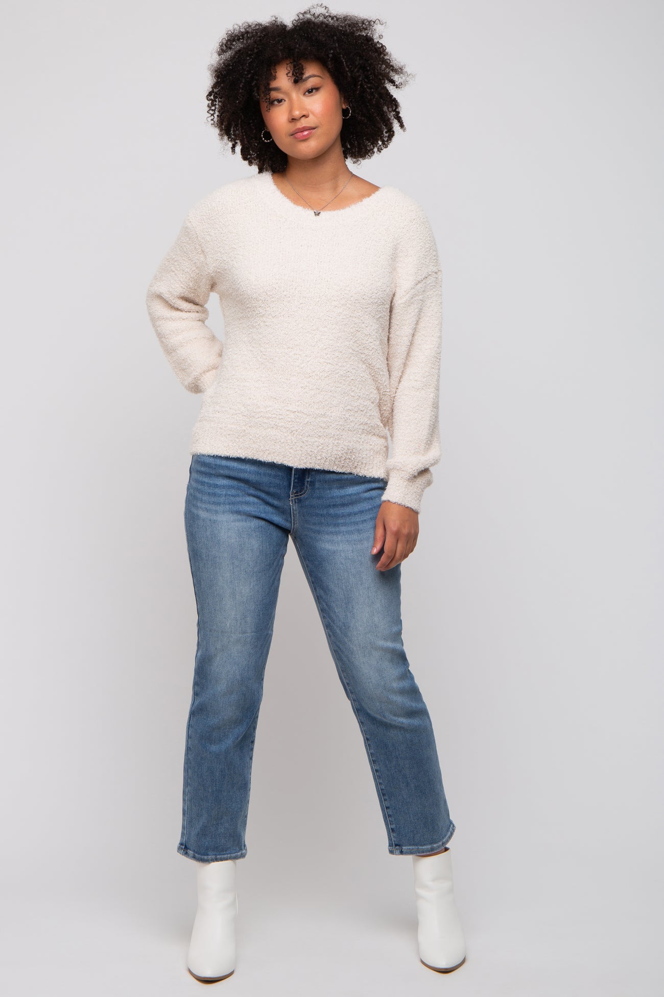 woman wearing a cream textured long sleeve sweater and light blue jeans with white ankle boots