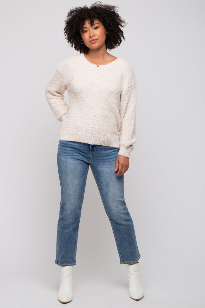 woman wearing a cream textured long sleeve sweater and light blue jeans with white ankle boots