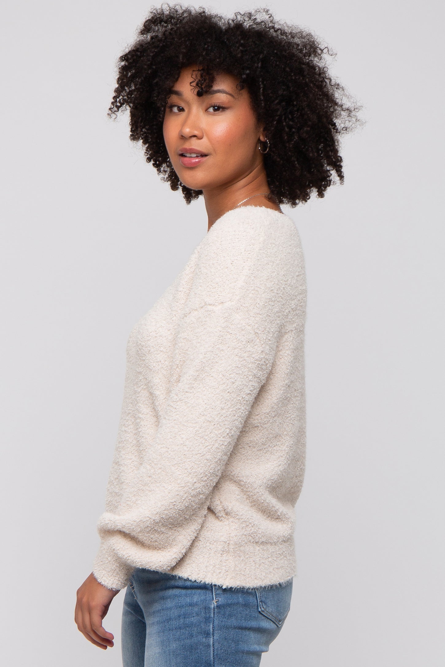 woman wearing a cream-colored textured sweater with a relaxed fit and long sleeves, paired with blue jeans