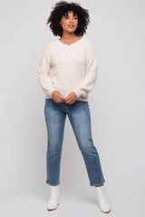 woman wearing a cream fuzzy oversized sweater and blue straight leg jeans with white ankle boots