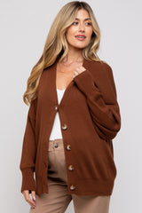 woman wearing a warm brown maternity cardigan with a relaxed fit and button details, styled over a white top