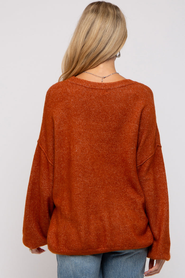 woman wearing an oversized rust orange maternity sweater, styled with slouchy sleeves and relaxed fit from the back
