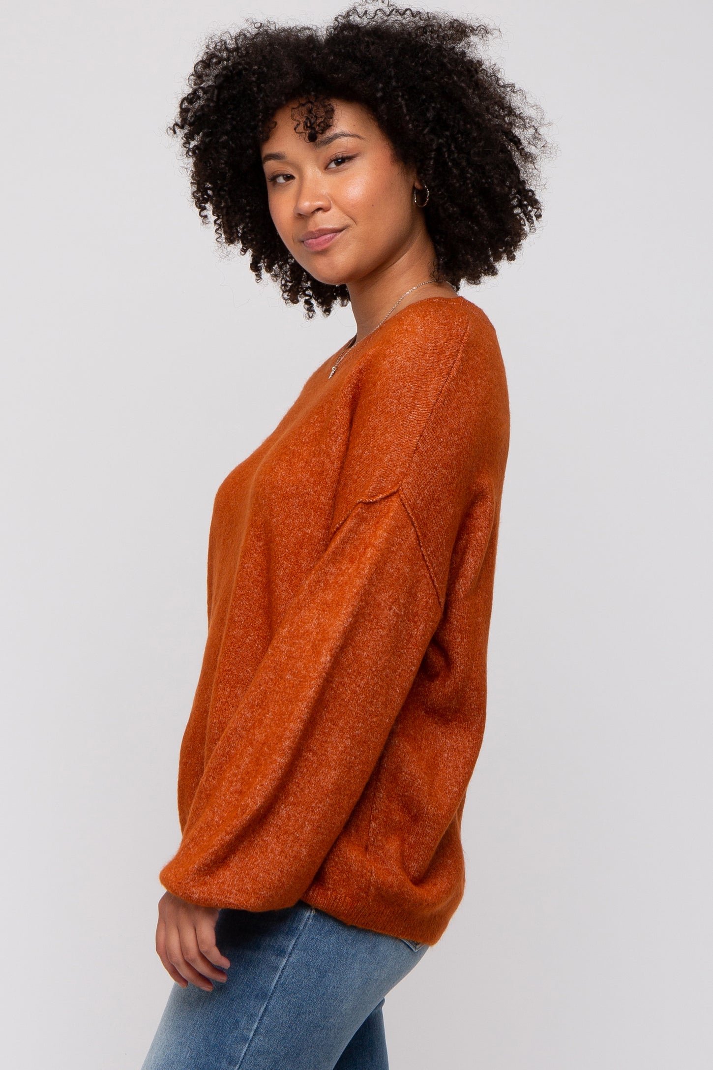 woman wearing an orange oversized sweater with long sleeves and a relaxed fit, paired with blue jeans