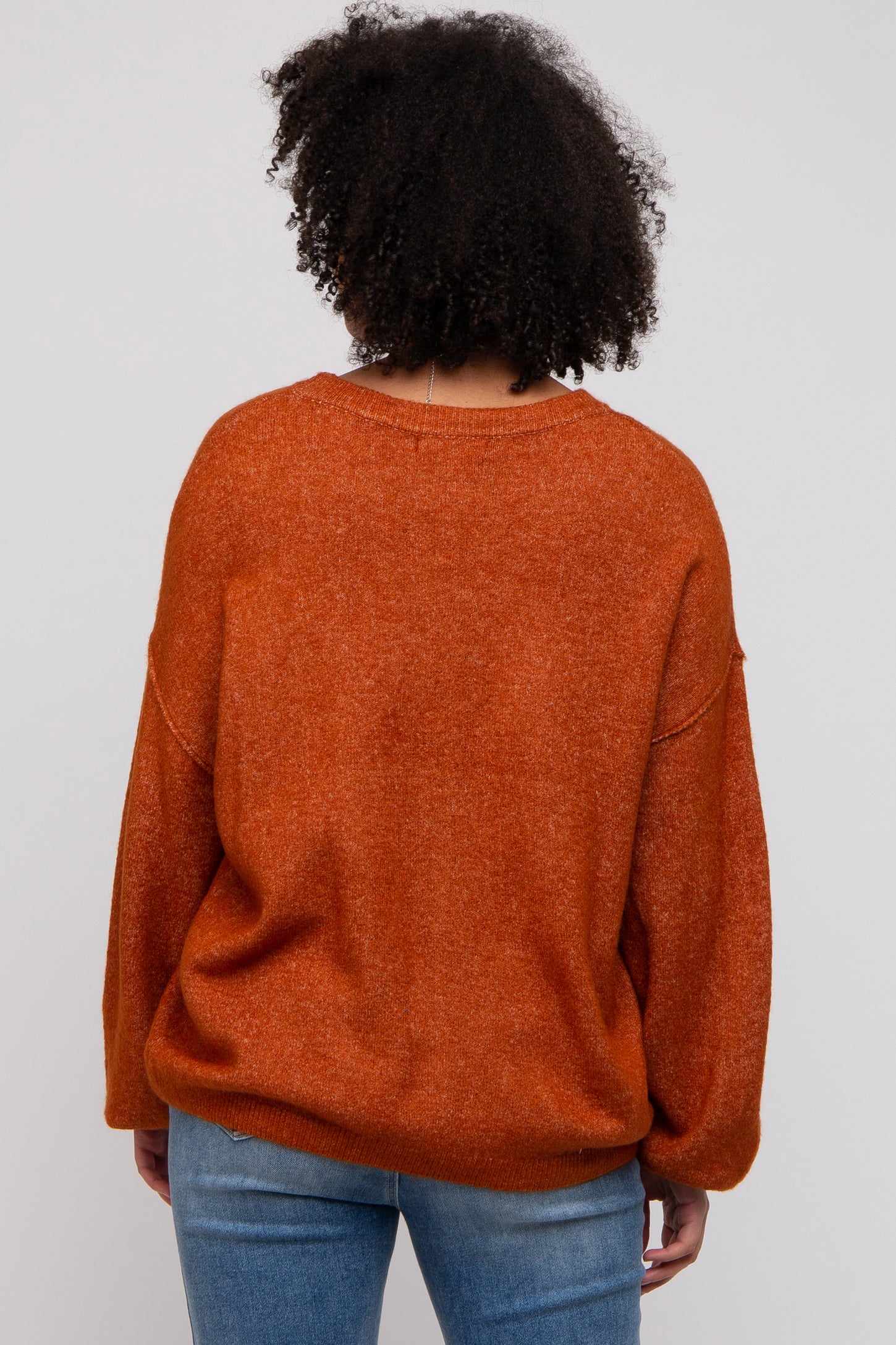 woman wearing an oversized orange sweater with a relaxed fit and long sleeves, viewed from the back
