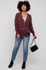 woman wearing a maroon oversized cardigan with buttons, gray top, and blue jeans, carrying a small black purse