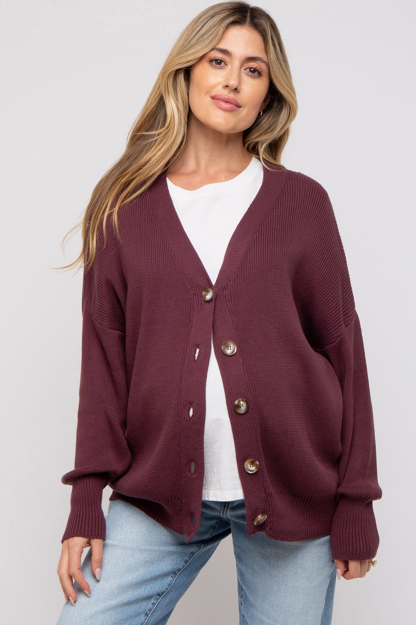 woman wearing a maroon maternity cardigan over a white top and light blue jeans