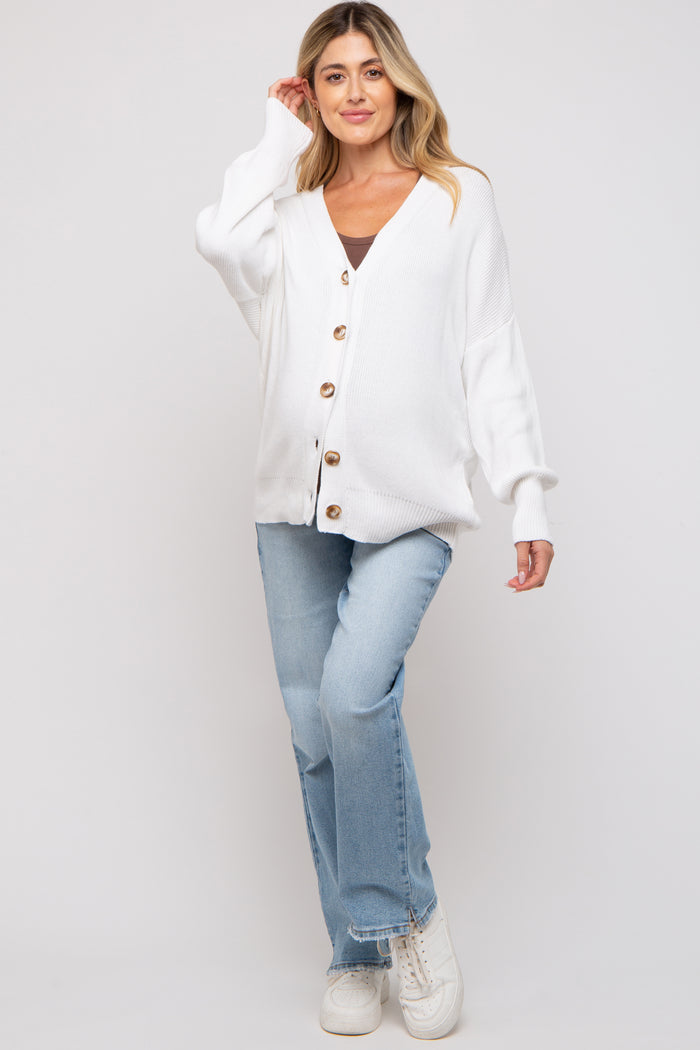 woman wearing a white button-up maternity cardigan over a black top and blue jeans, smiling at the camera