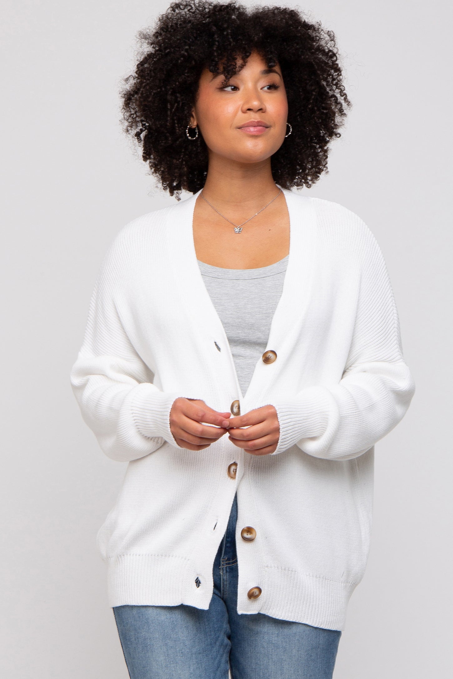 woman wearing a white oversized cardigan with wooden buttons over a gray top and blue jeans
